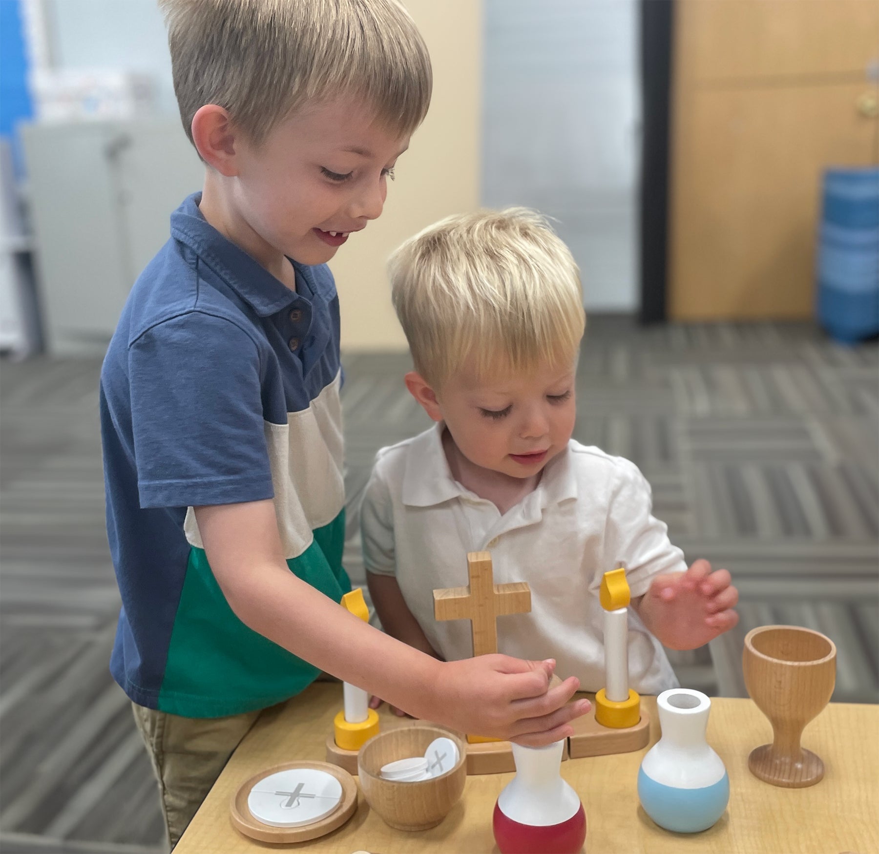 two young boys playing with wooden catholic mass set