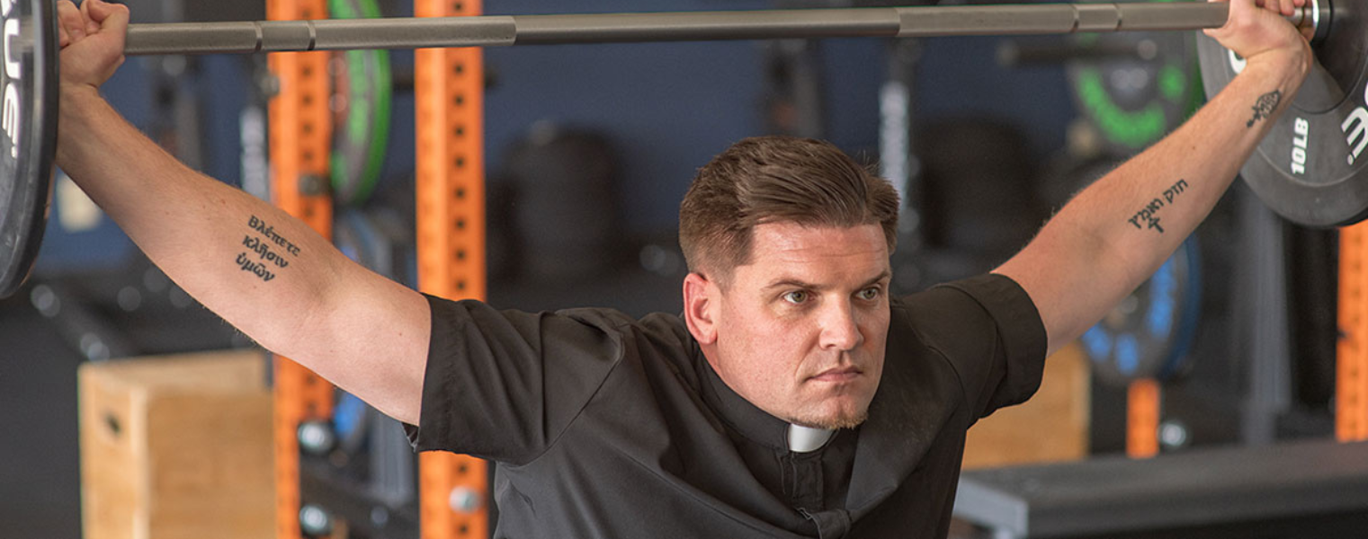 a man pressing a barbell above his head  wearing a short sleeve performance clerical shirt