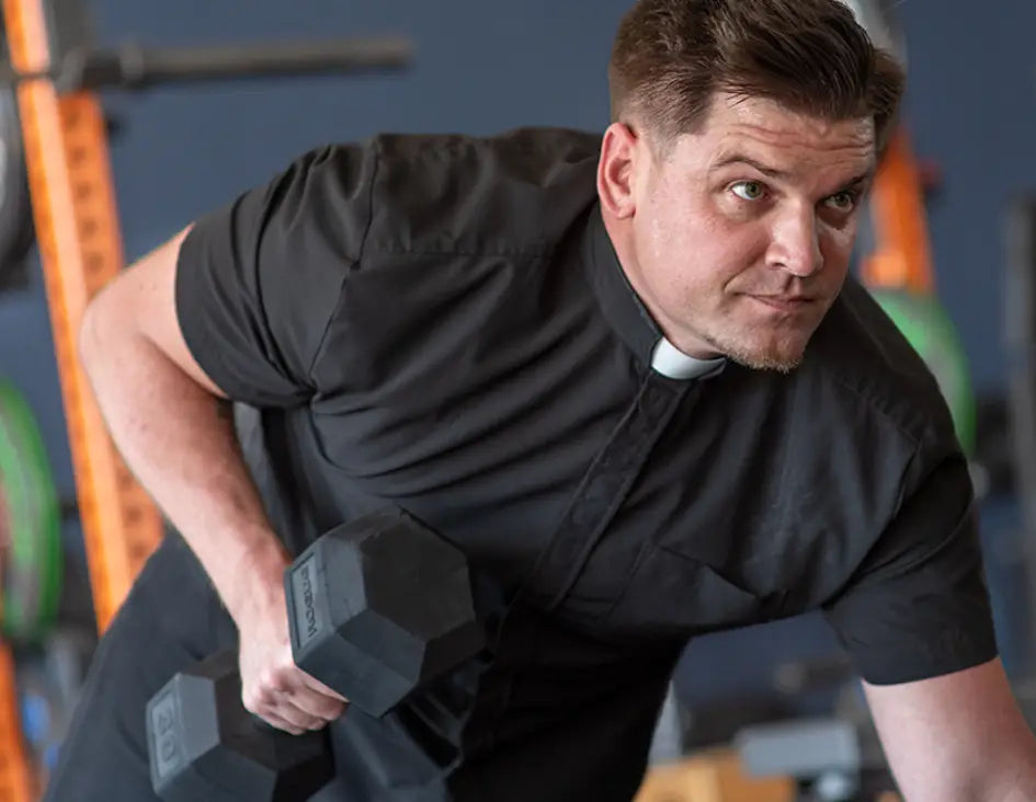 man in gym lifting weight whilst wearing a performance short sleeve clerical shirt from wicking vicar